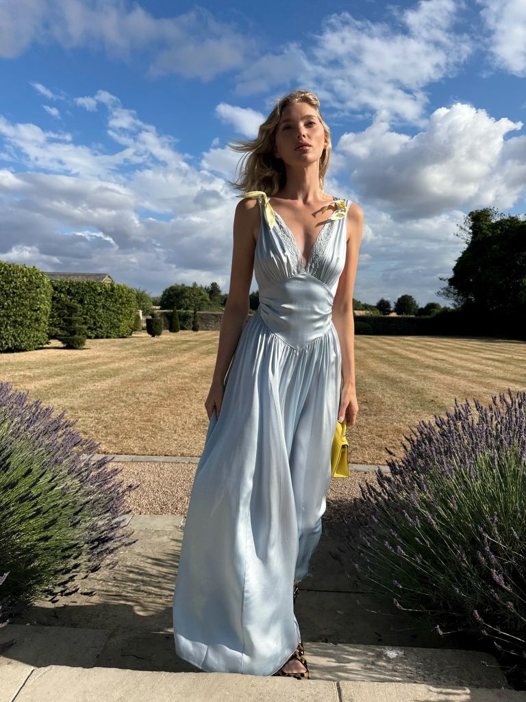 Elsa Hosk dans sa robe en soie jaune bleu et beurre debout dans un champ entouré de buissons topiaires et lavande