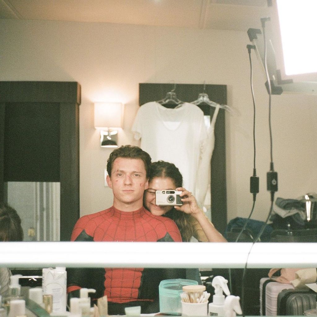 Tom Holland and Zendaya dressed as their spiderman characters photographed by Zendaya for a mirror selfie in an onset trailer
