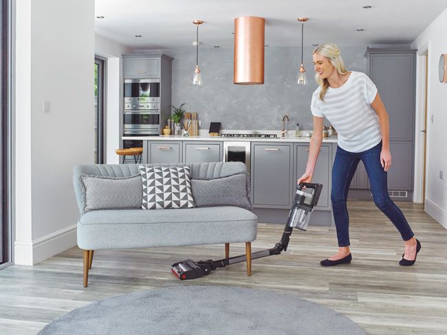 woman vacuuming under small grey sofa