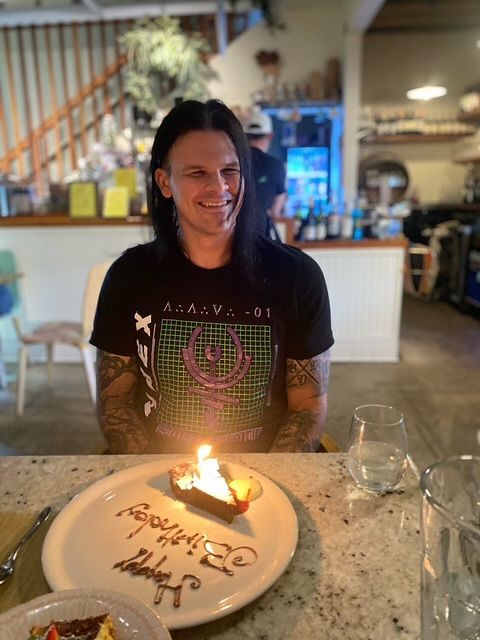 Travis Bacon posa para uma foto dentro de sua casa de família com uma fatia de bolo de aniversário, compartilhada no Instagram