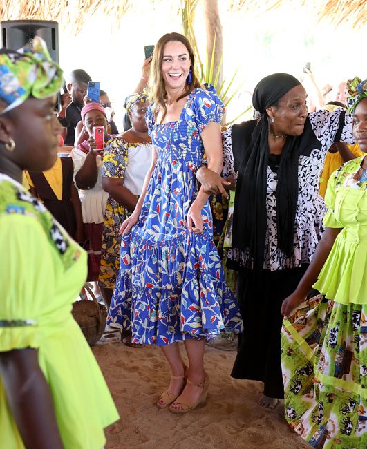 kate wears a bright blue tiered frilly midi length dress that is decorated with red and white flowers and she holds it as she dances in cream wedge sandals
