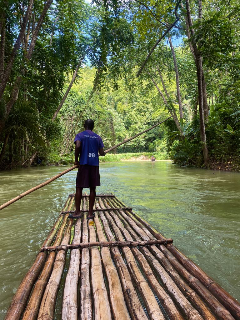 long bamboo raft on a canal of water with man in shorts standing on top