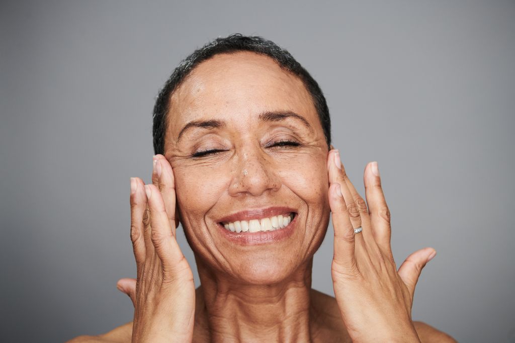 Close-up beauty portrait of a happy, healthy mature woman touching her face with her hands.