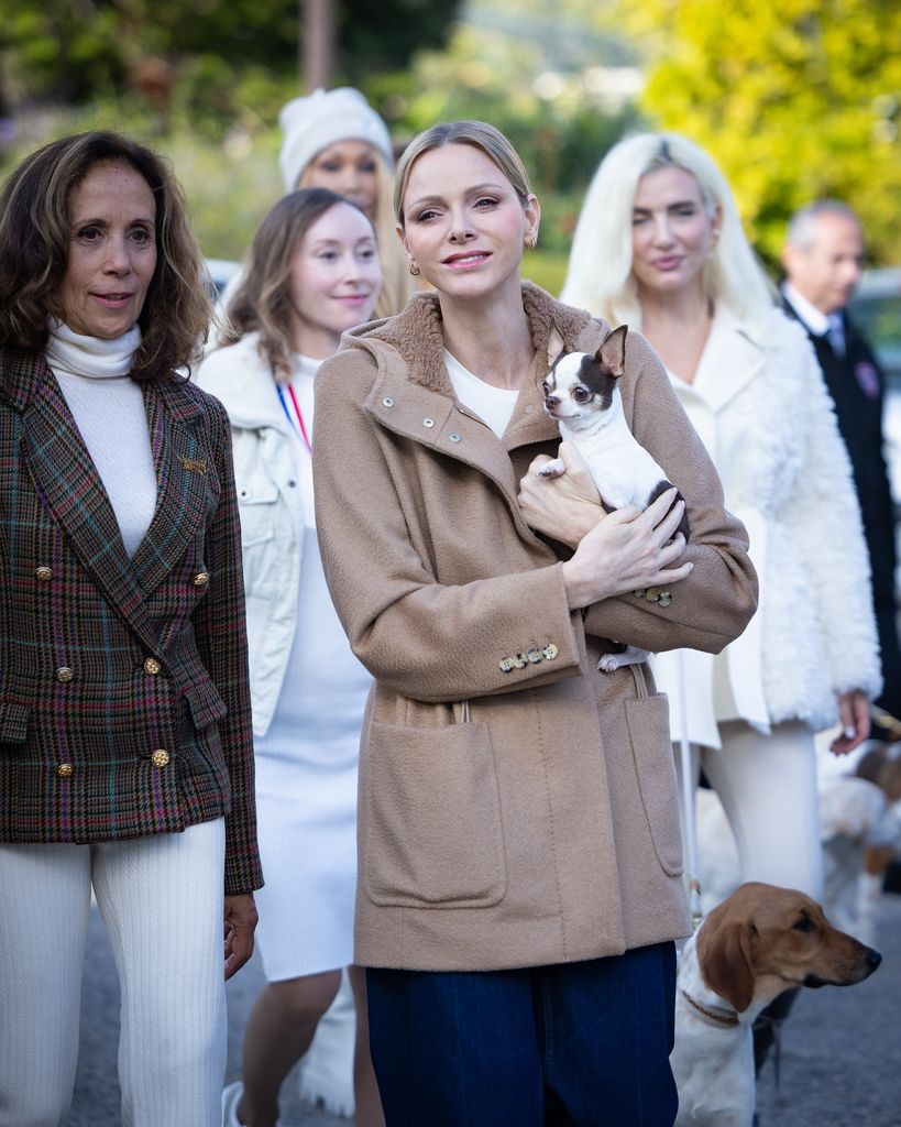 Princess Charlene in jeans with a tan coat holding chihuahua