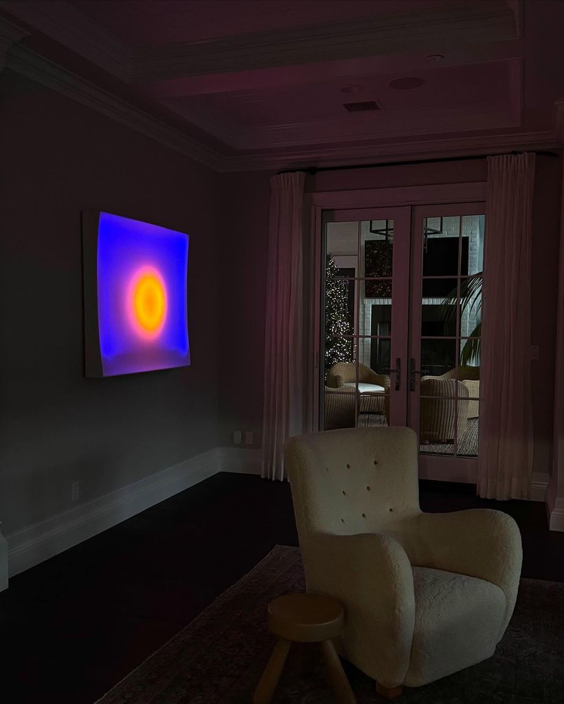 A glowing blue and orange piece of art on a wall with a white chair in front of it 