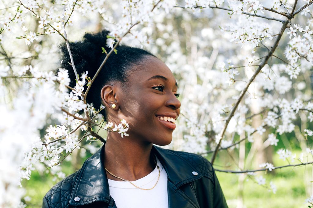 Beautiful young black girl smiling against blossom spring trees outdoors.