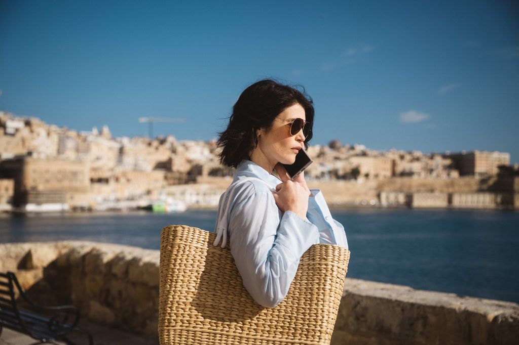 woman carrying beach bag and talking on phone in sunny location