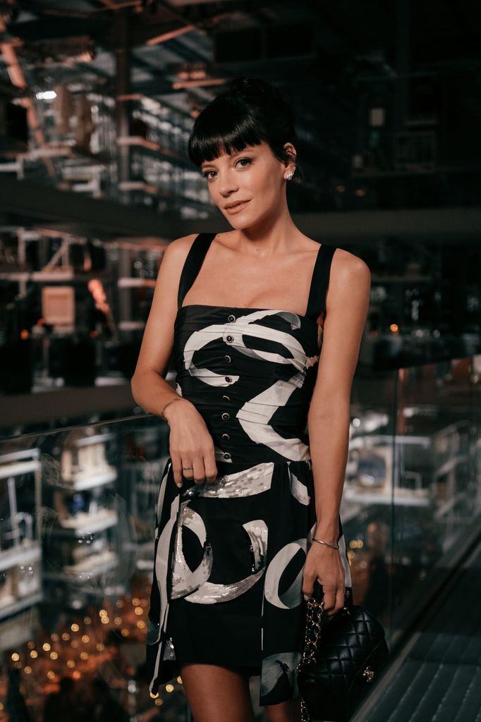  Lily Allen stands poised in a Chanel mini dress printed with abstract black and white brushstrokes and sequin accents, accessorised with a quilted Chanel bag, as she attends the house’s 100-year celebration at the V&A East Storehouse.