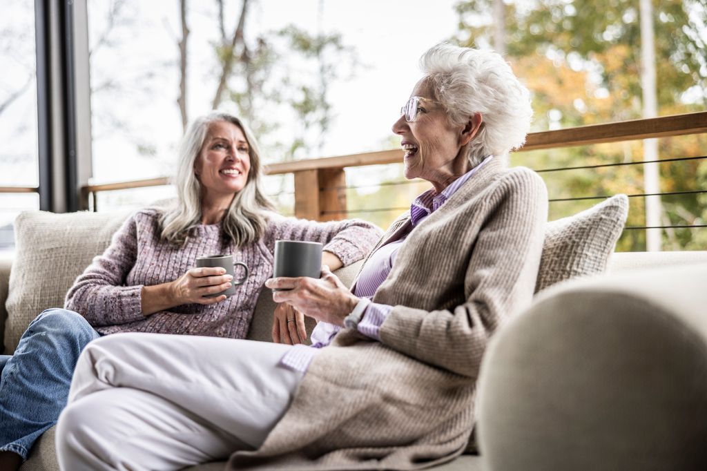 Senior mother and daughter having coffee and talking on back porch of vacation home