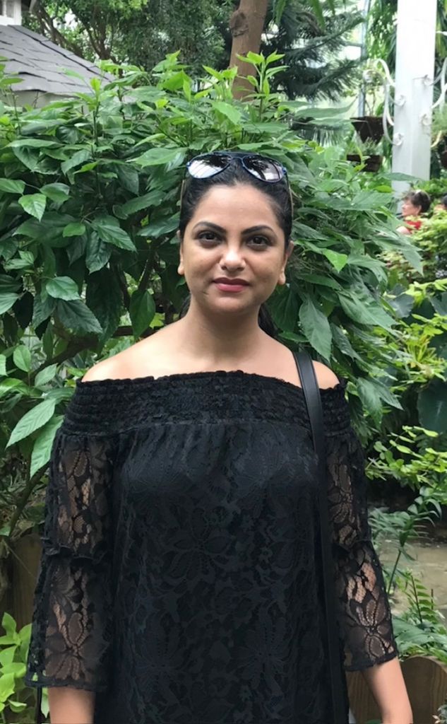 Rajni in black dress in front of hedge