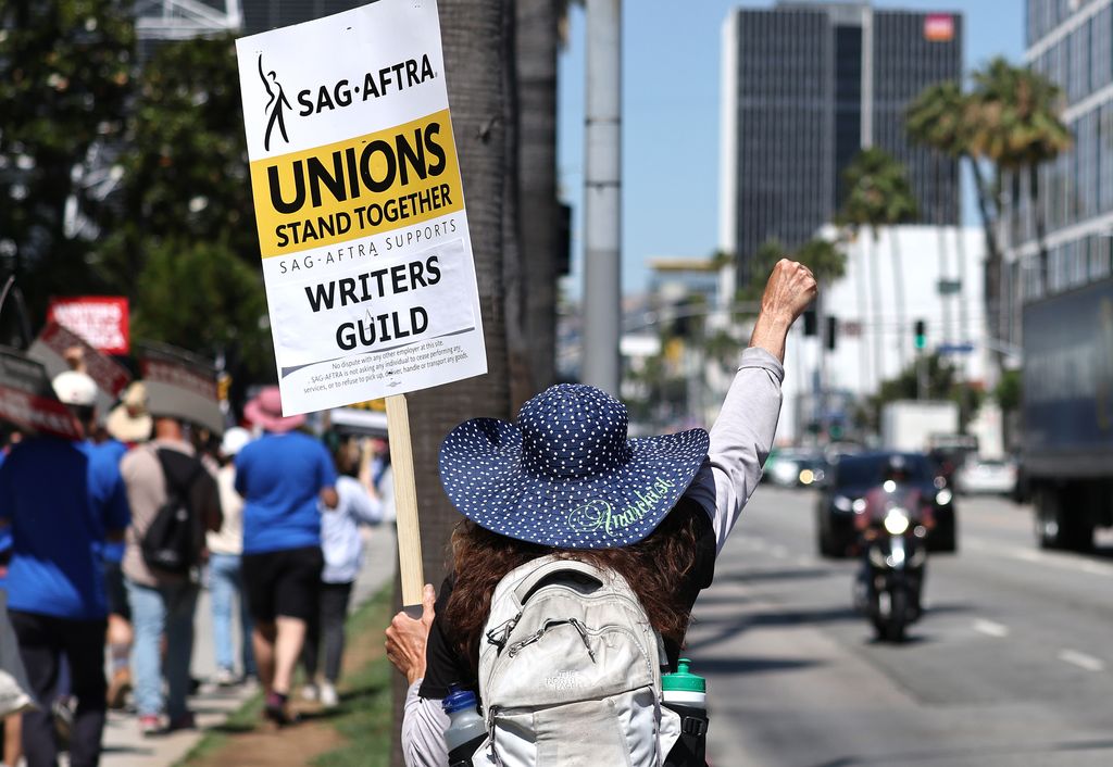 A sign reads 'Associations Stand Together' as members of SAG-AFTRA walk on the fence to show solidarity with the WGA (American Writers Association) staff on strike. public outside the Netflix office on July 12, 2023 in Los Angeles, California