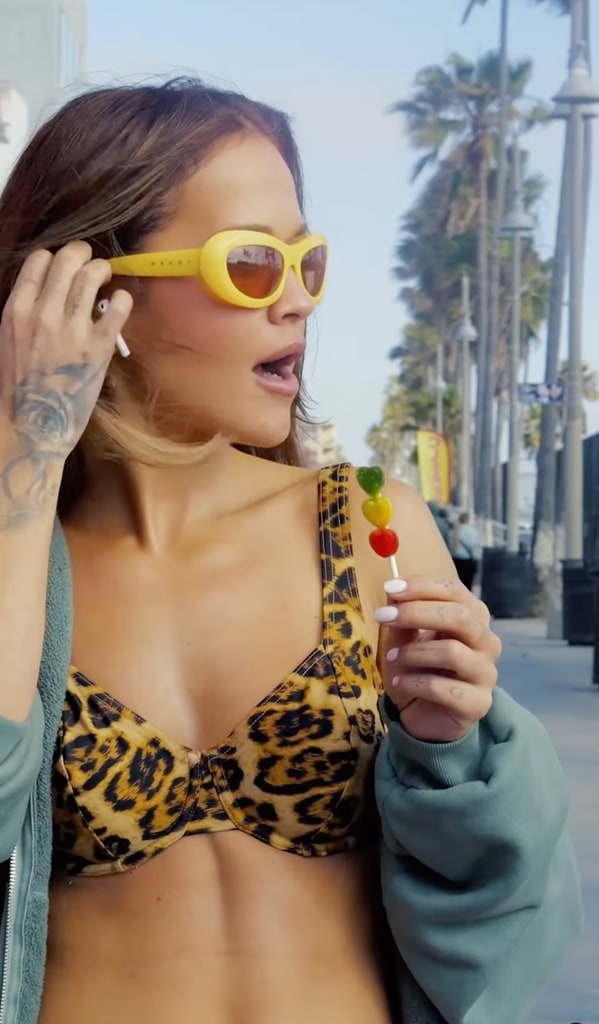 Rita Ora tucks a piece of hair behind her ear. She carries her lollipop and listens to music in her Air Pods as she strolls down a Californian street. 