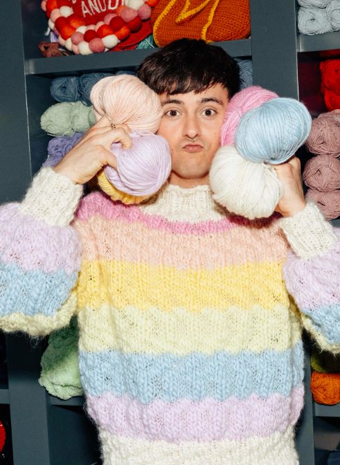 Tom Daley in a colourful knitted jumper holding balls of yarn