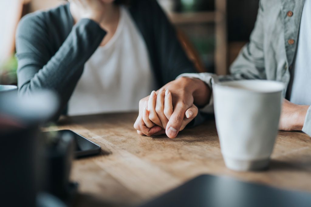 Close up of young Asian couple on a date in cafe, holding hands on coffee table. Two cups of coffee and smartphone on wooden table. Love and care concept