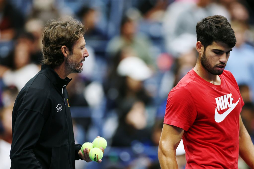 Carlos Alcaraz of Spain in red nike top talks with his coach Juan Carlos Ferrero during a practice session ahead of the 2025 US Open 