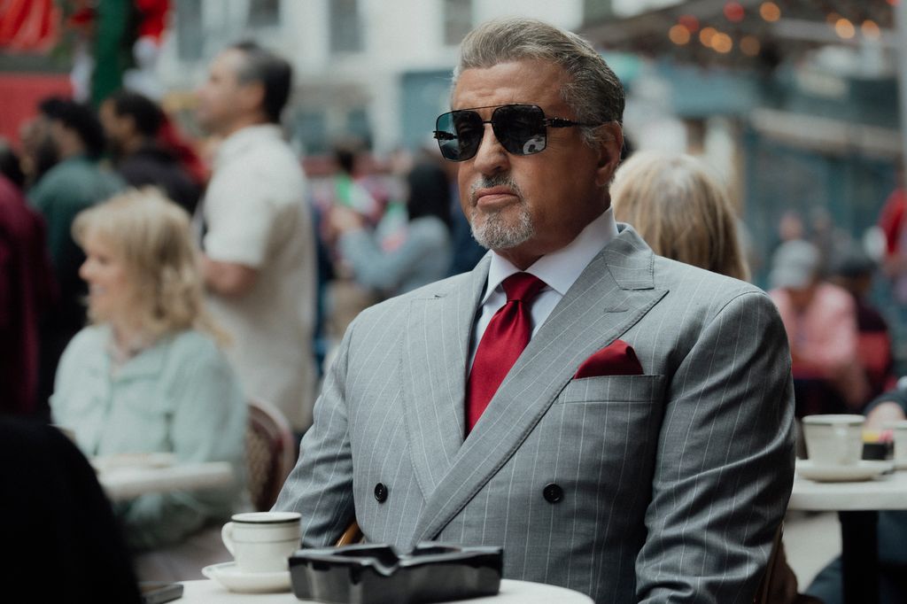 man in grey suit and glasses sitting at cafe table outdoors