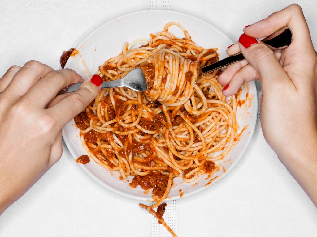A bowl of spaghetti bolognese being eaten with a fork and spoon