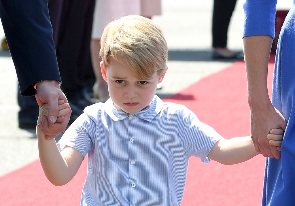 A young Prince George holding the hands of Prince William and Kate Middleton