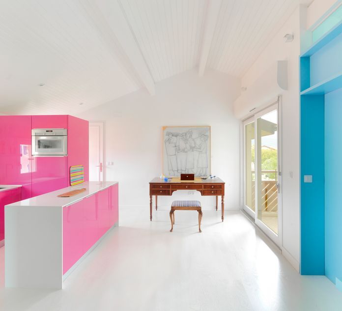 A minimalist, bright white interior by Pía López-Izquierdo Botín showcasing a high-gloss hot pink kitchen island and cabinetry