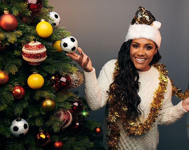 Alex Scott in a Christmas hat posing next to a Christmas tree