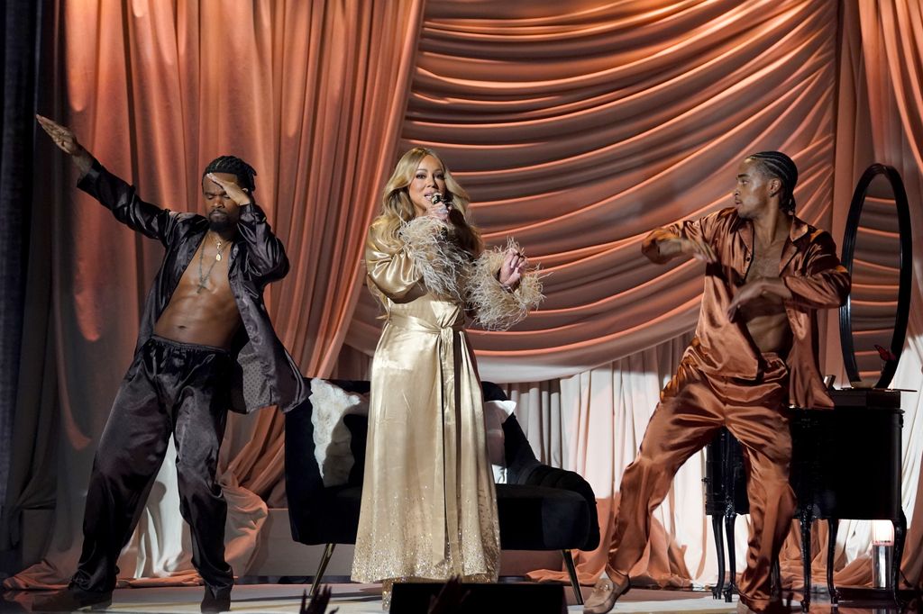 Mariah performs onstage in a silk champagne-colored robe with two of her dancers.
