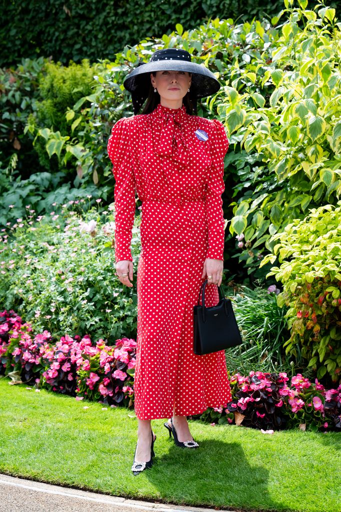 Flora Macdonald Johnston wears a red and white polka dot midi dress with a black wide-brim hat and matching handbag at Royal Ascot - (wearing a Lock & Co hat, The Irish Twin dress, Swaine bag and Manolo Blahnik shoes)