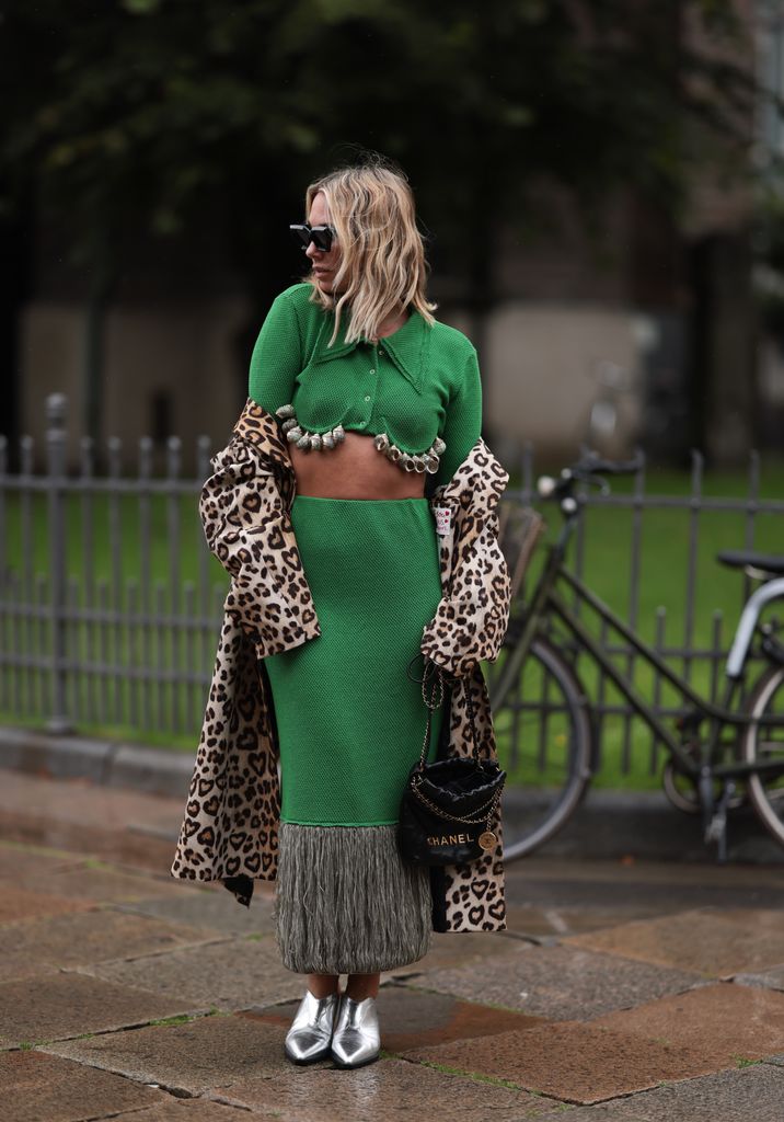 Karin Teigl seen wearing Louis Vuitton black sunglasses, Milk White green two-piece / green cropped collar knit cardigan with long sleeves and shell details and matching green knit long skirt with fringe details, H&M beige / brown leopard / animal pattern long coat, Chanel 22 black leather bag, Copenhagen Studios silver metallic boots, during the Copenhagen Fashion Week Spring/Summer 2024 on August 09, 2023 in Copenhagen, Denmark. (Photo by Jeremy Moeller/Getty Images)