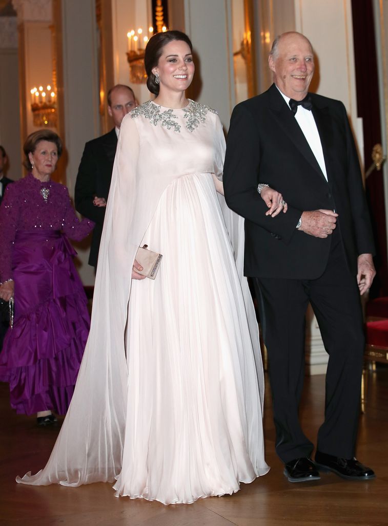 kate in caped pale gown is escorted into dinner by King Harald V of Norway at the Royal Palace