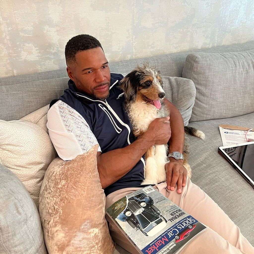 Michael Strahan sat on a couch looking off into the middle distance with his dog Zuma doing the same while held at his side
