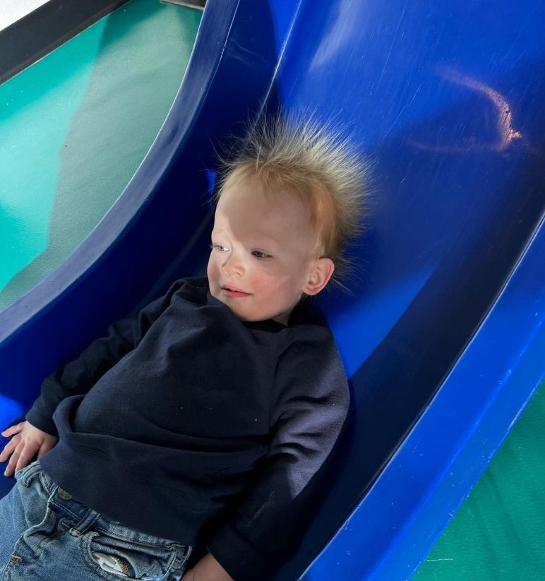 A child with static hair on a blue slide