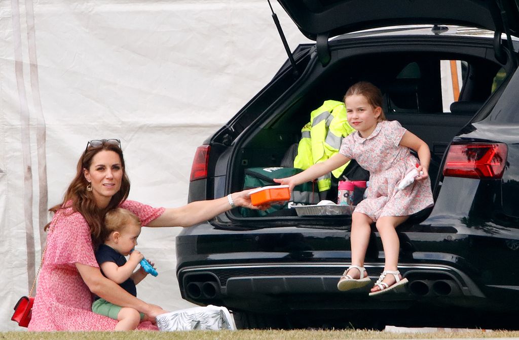 Princess Kate in a pink dress handing a lunchbox to Princess Charlotte 