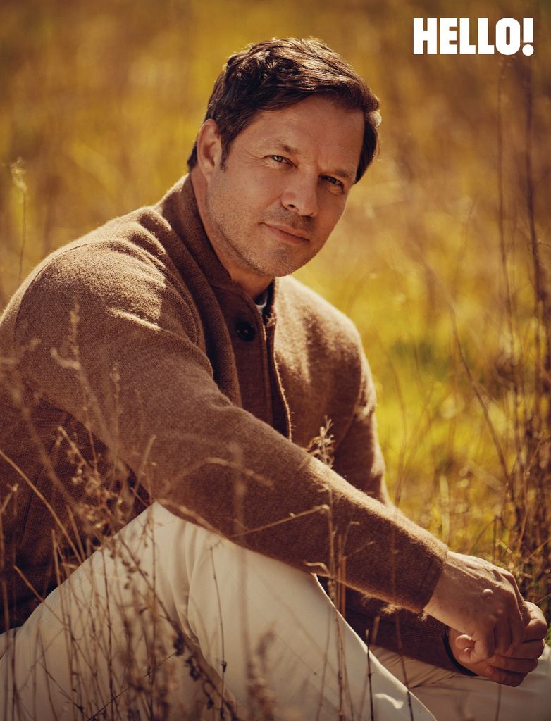 A man in a field wearing a long brown jumper and light brown trousers