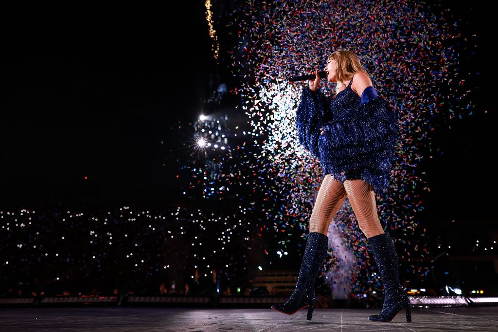 Taylor swift on stage wearing a sparkly pink bodysuit with sparkly blue  boots on Craiyon