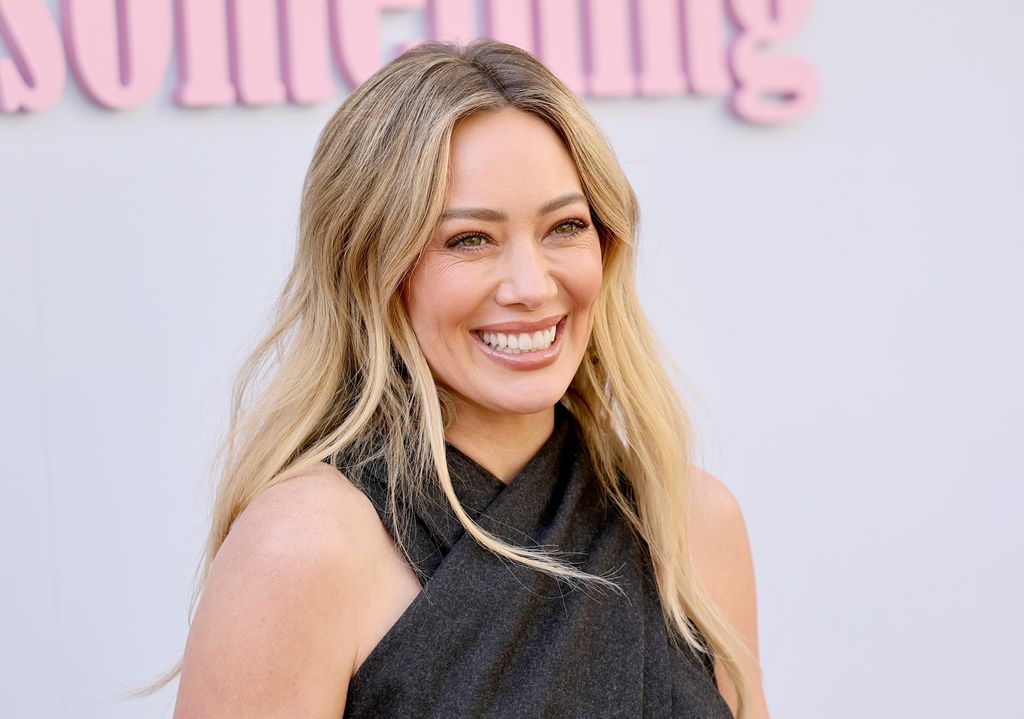 Hilary Duff sourit à la caméra dans une robe portefeuille dos nu.