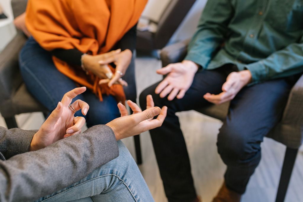 Detailed crop of hands gesturing of anonymous husband and wife sharing marriage problems with therapist on psychology session