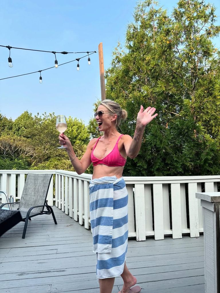 Amy Robach poses in a bikini with a glass of wine on the deck of her beach house on a family vacation to Montauk, shared on Instagram
