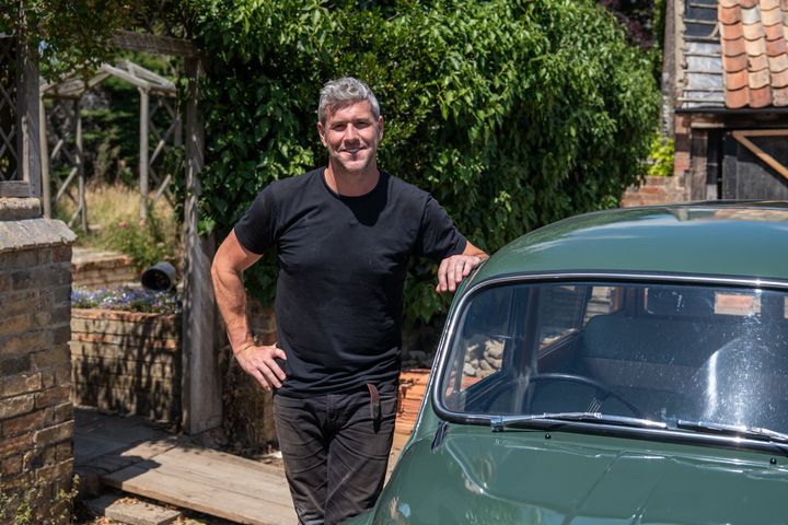Ant Anstead in black t-shirt posing next to green car