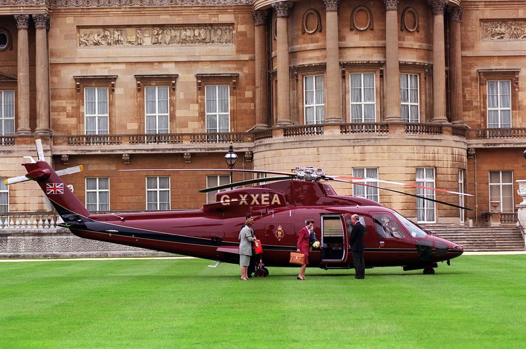A red helicopter landing on grass outside of the palace