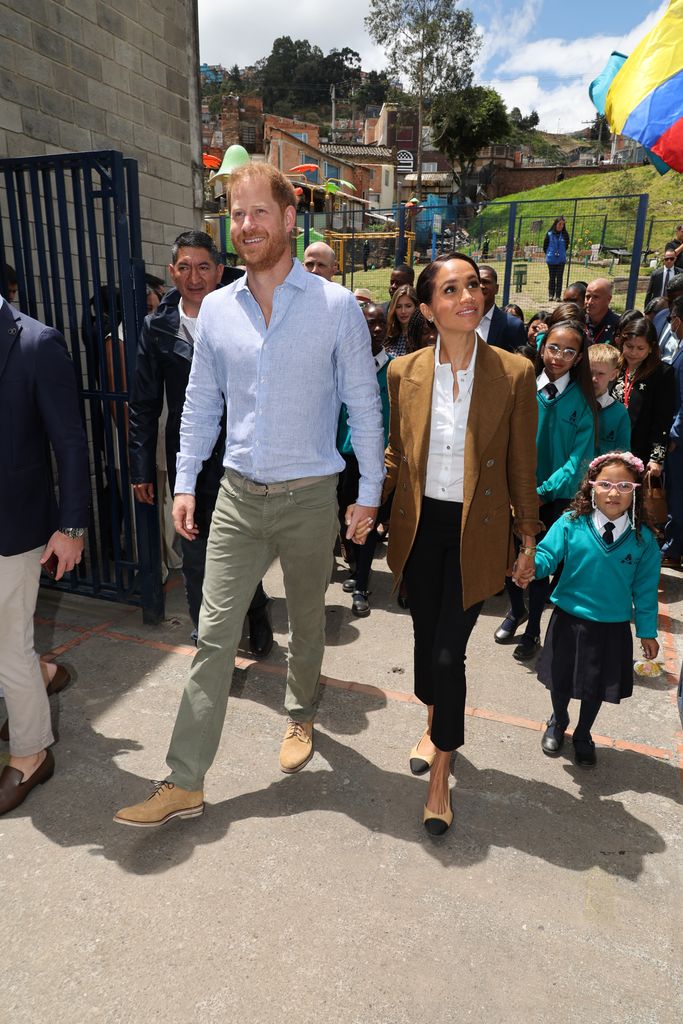 Prince Harry and Meghan Markle walking through a school with children