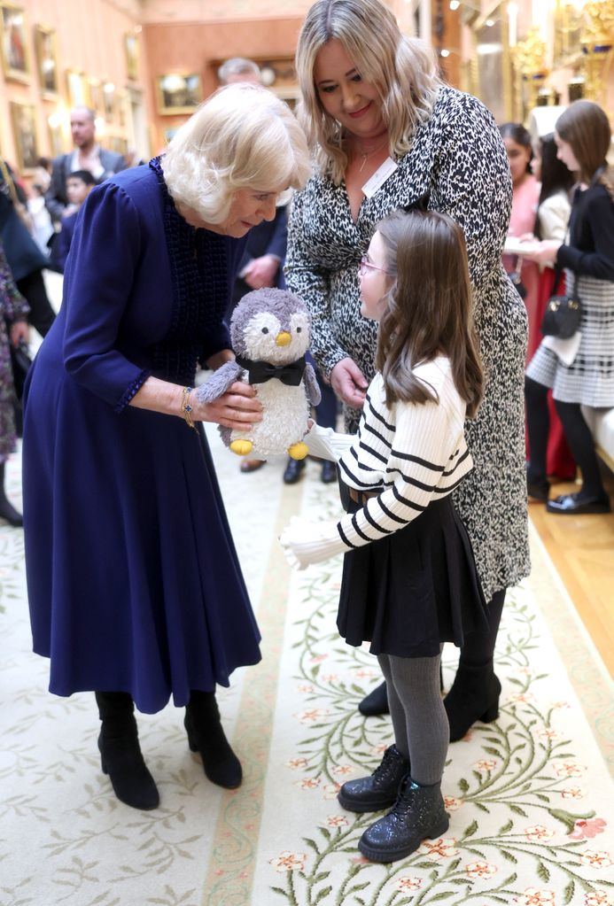 Queen Camilla with a young child and a stuffed penguin toy