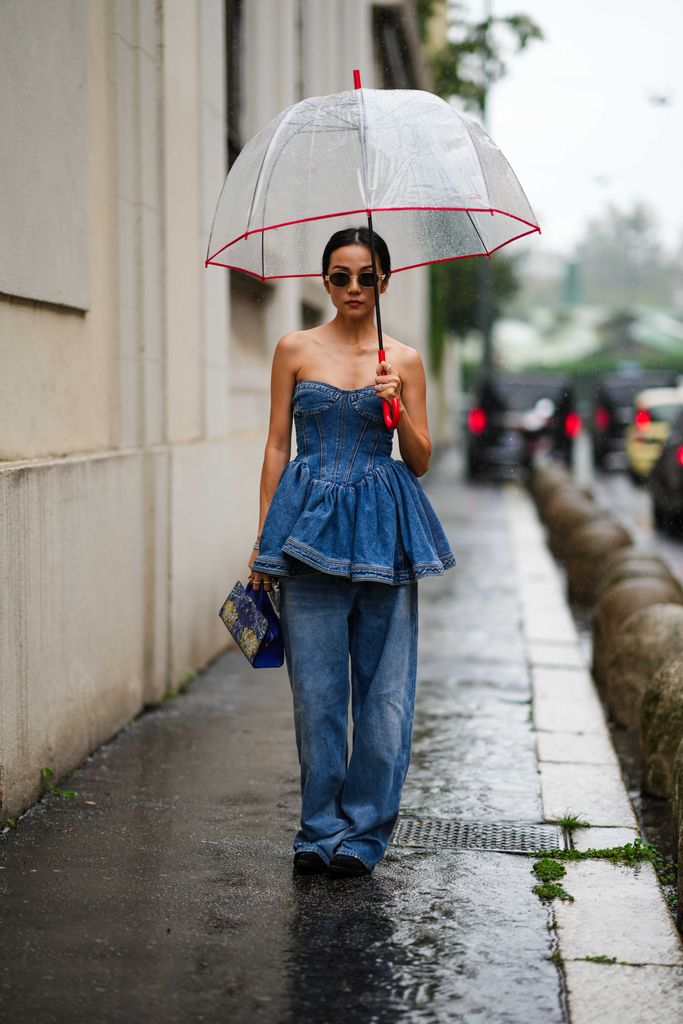 MILAN, ITALY - SEPTEMBER 21: Yoyo Cao wears sunglasses, a blue denim low-neck off-shoulder ruffled top, blue wide-leg flared denim jeans / pants, a bag, outside Aigner, during the Milan Fashion Week - Womenswear Spring/Summer 2024 on September 21, 2023 in Milan, Italy. (Photo by Edward Berthelot/Getty Images)