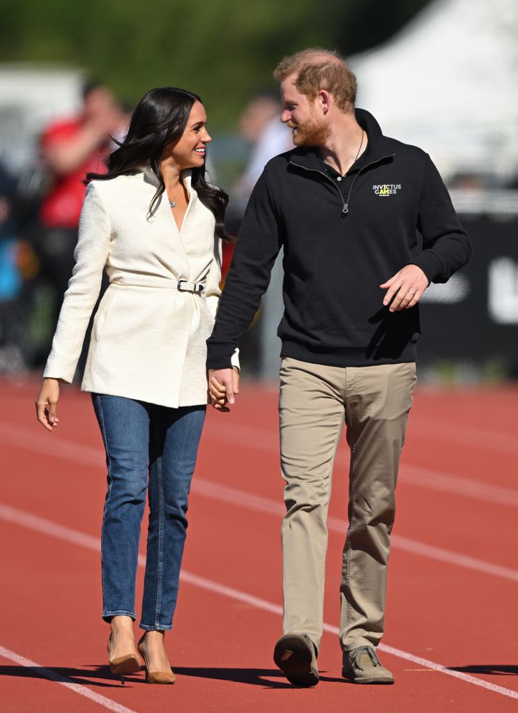Meghan Markle and Prince Harry walking hand-in-hand on an athletics track