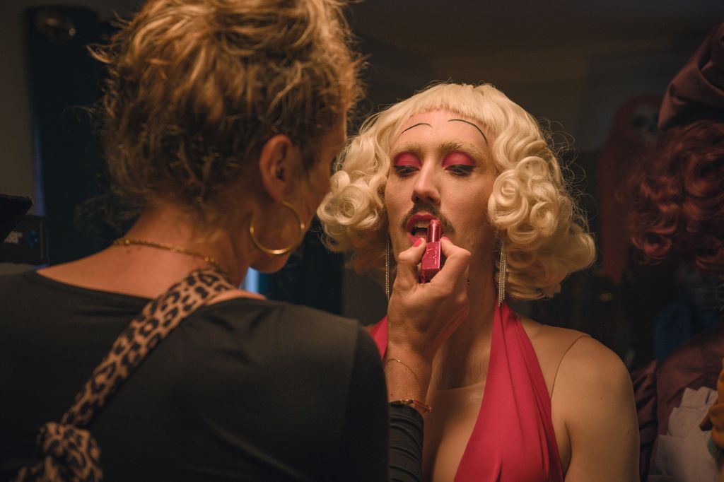 woman putting lipstick on another person in blonde wig