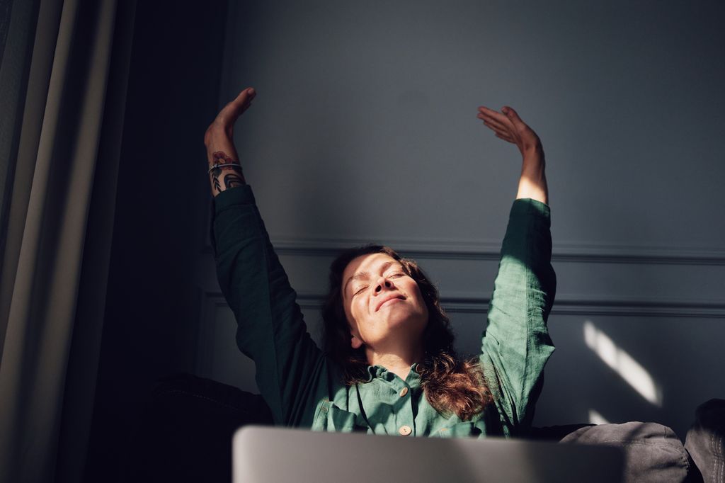 Woman raising arms and enjoying sunlight indoors. Joyful and relaxed atmosphere.