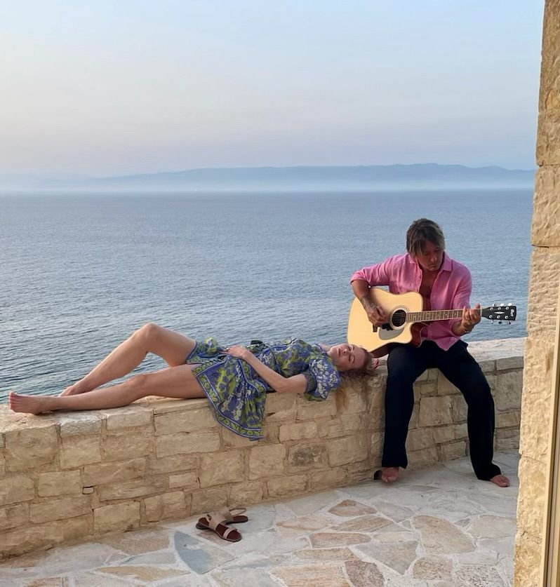 Nicole Kidman lying on a stone wall while Keith Urban plays the guitar