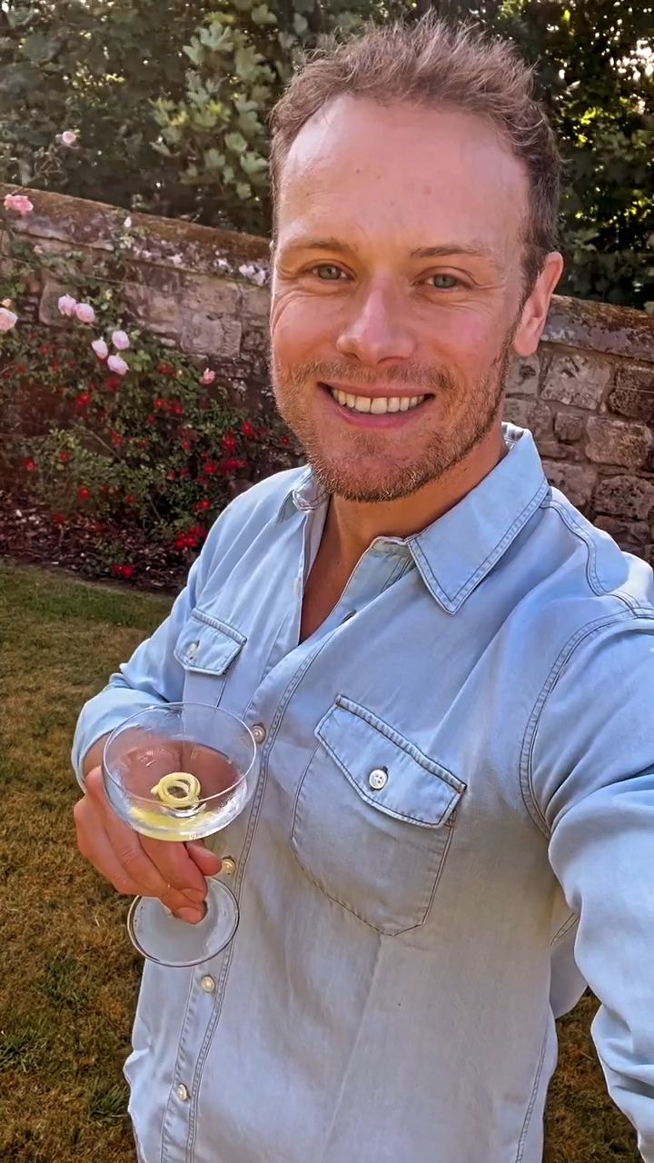 Sam Heughan holding a cocktail in a walled garden