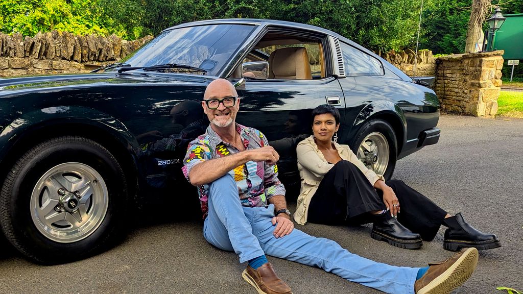 Man and woman sitting on ground in front of classic car