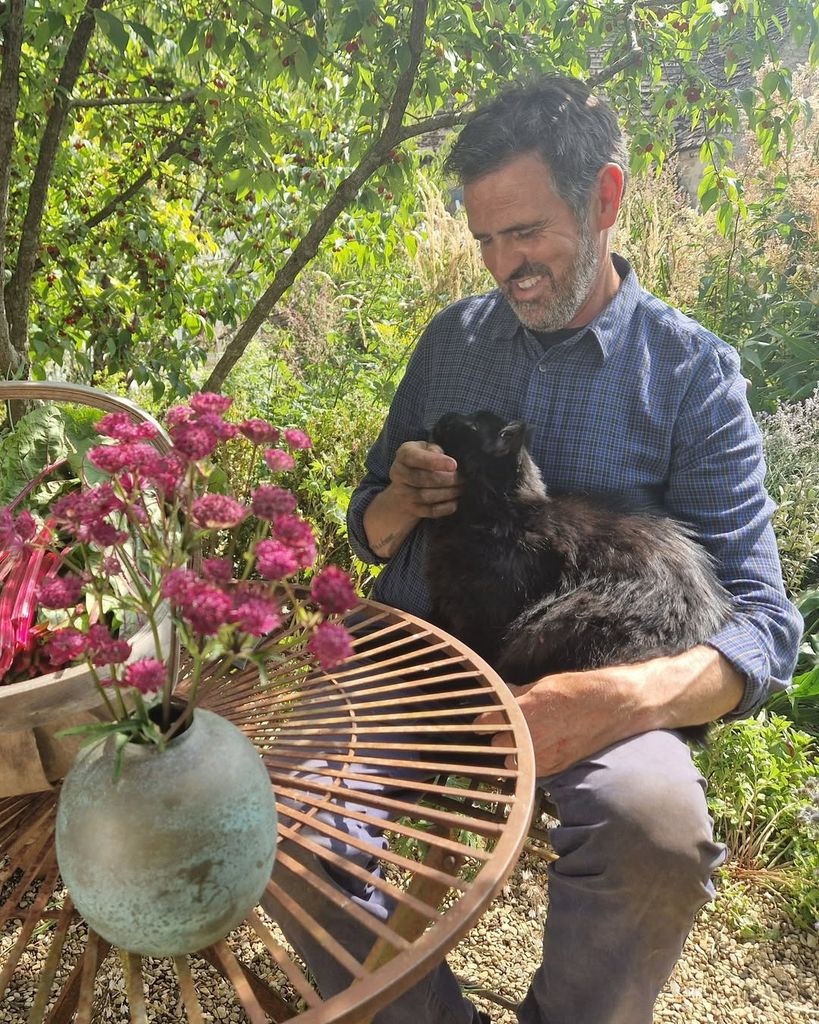 Adam Frost cuddling his cat sitting on garden furniture