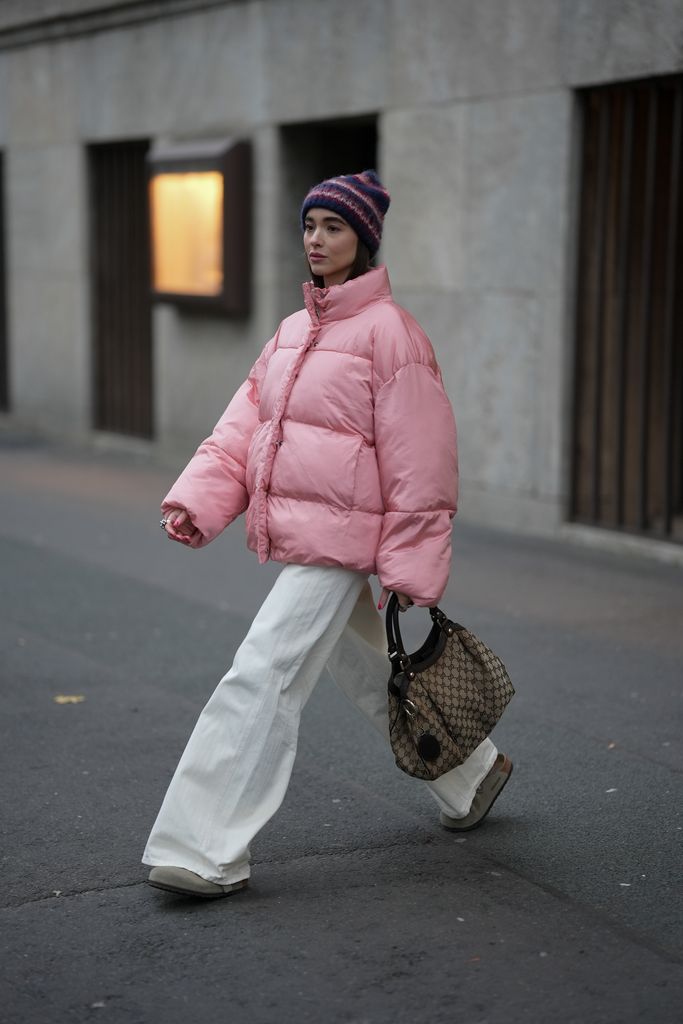  Evi Wave is seen wearing an oversized puffer jacket in a soft pink rose tone with a high collar and voluminous, boxy silhouette from American Vintage; cream white wide-leg jeans with subtle stripes from Replay; taupe-grey Boston clogs in soft suede with an open back and adjustable strap from Birkenstock; a vintage Gucci shopper hobo bag in beige canvas 