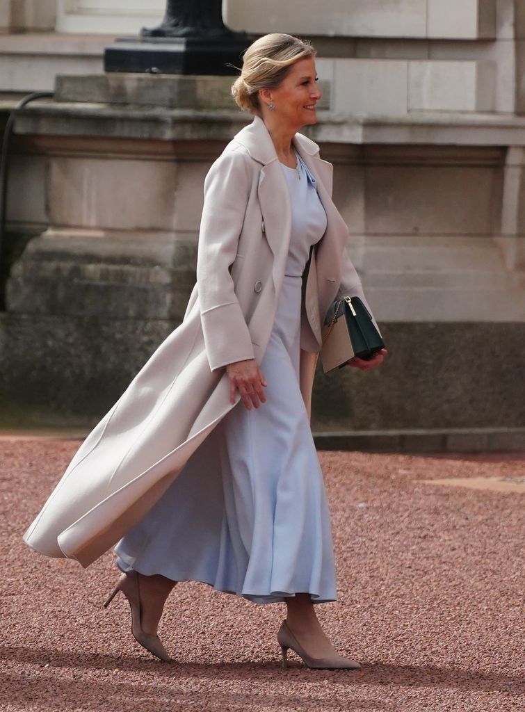 Sophie from side in blue dress and cream coat